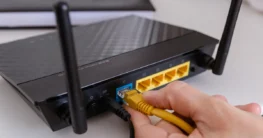Hand steckt ein Kabel in die Anschlüsse auf der Rückseite eines Routers