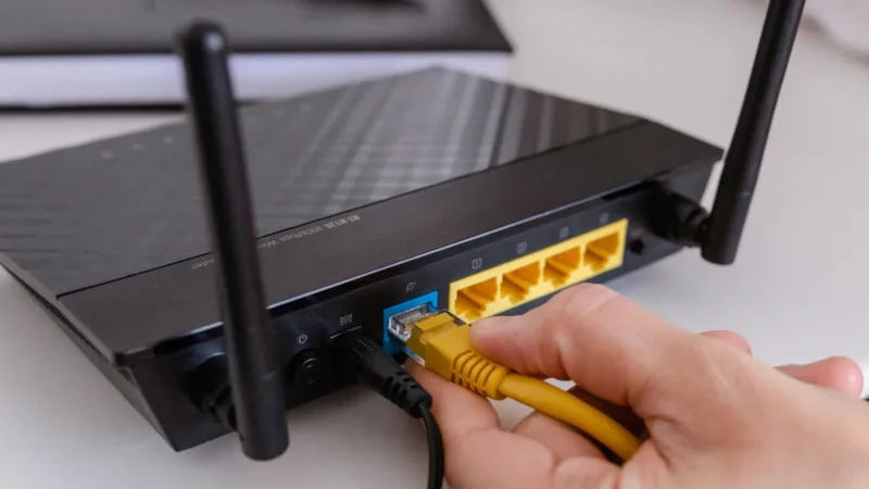 Hand steckt ein Kabel in die Anschlüsse auf der Rückseite eines Routers