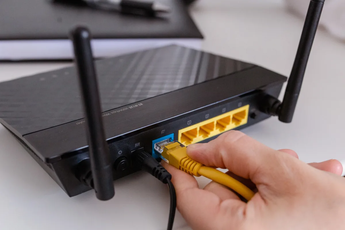 Hand steckt ein Kabel in die Anschlüsse auf der Rückseite eines Routers