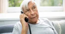 Älterer Mann telefoniert zu Hause mit einem schnurgebundenen Festnetztelefon