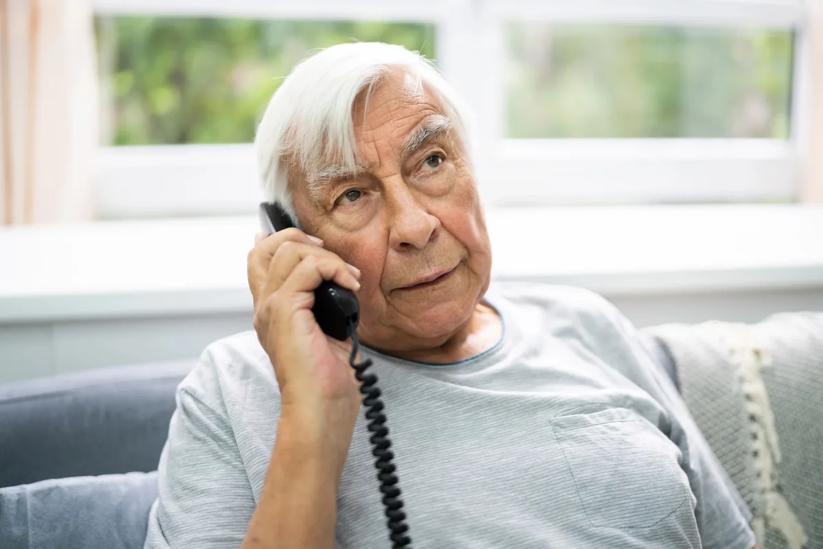 Älterer Mann telefoniert zu Hause mit einem schnurgebundenen Festnetztelefon