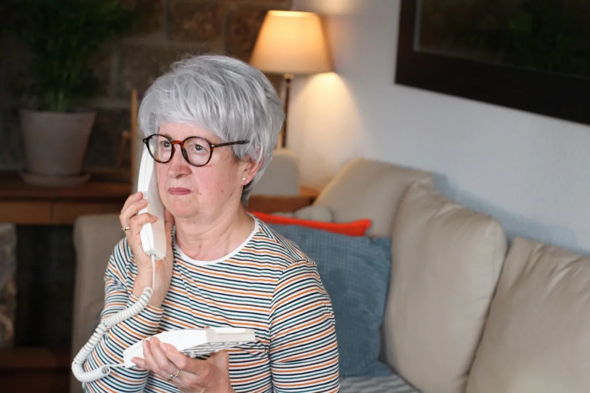 Seniorin telefoniert auf dem Sofa mit einem schnurlosen Festnetztelefon